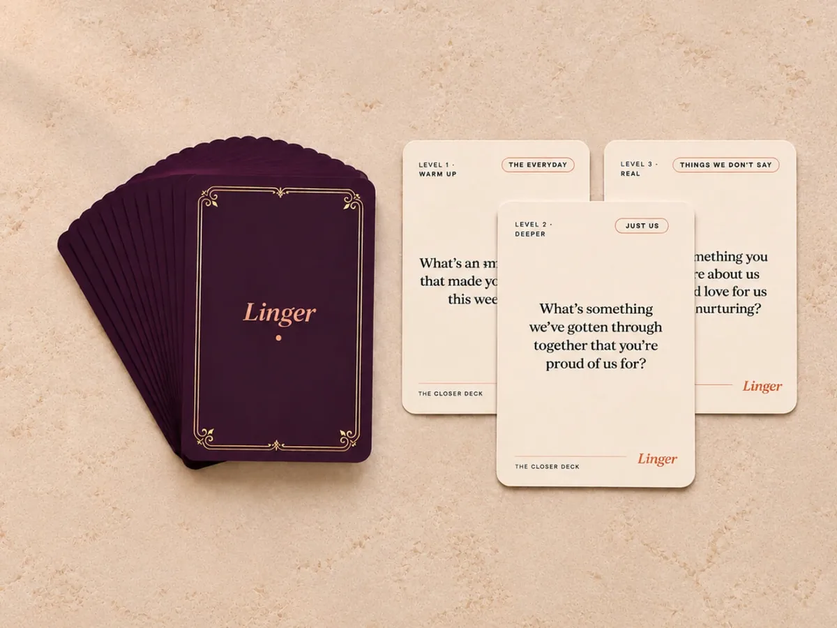 The Linger Closer Deck — a stack of plum conversation cards with gold detailing beside three cream question cards on a soft neutral surface.